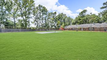 A large grassy field with trees in the background and a building to the right.